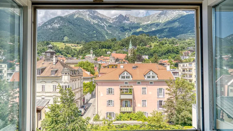 Panoramablick aus dem Fenster auf die Stadt und die majestätischen Berge im Hintergrund.