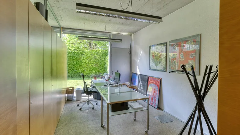 Helles Büro mit großen Fenstern, Blick ins Grüne und integrierten Holzschränken.