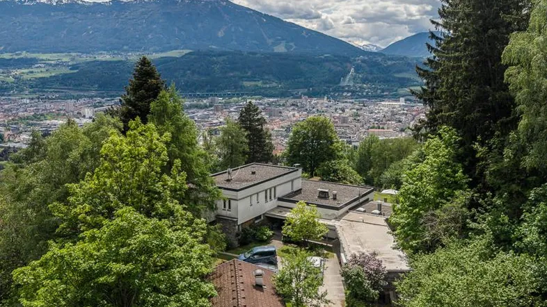 Luftaufnahme eines Hauses umgeben von Bäumen mit Stadt- und Bergblick im Hintergrund.