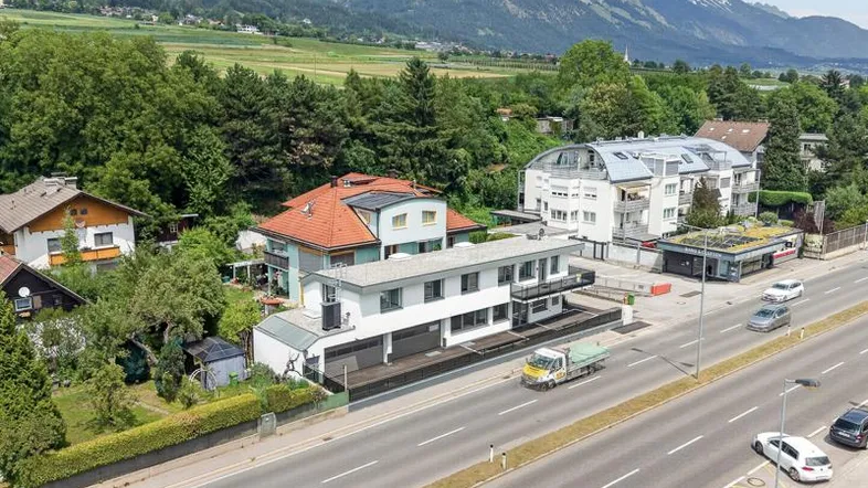 Luftaufnahme eines modernen Gebäudes an einer Straße mit Bergpanorama im Hintergrund.