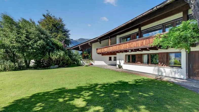Gepflegter Garten mit großer Rasenfläche, Balkon und Bergblick unter blauem Himmel.