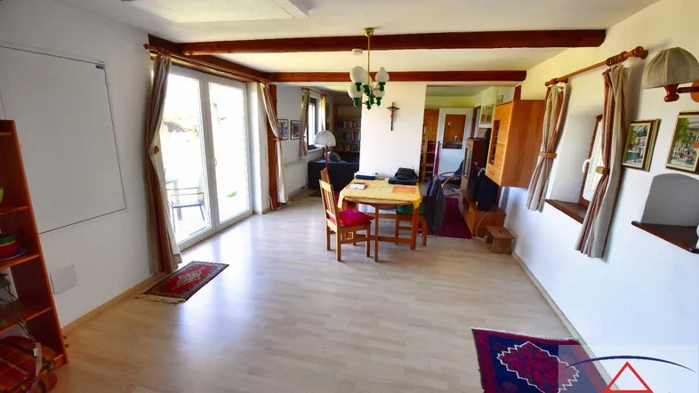 Geräumiger Wohn- und Essbereich mit hellem Holzboden, sichtbaren Holzbalken und Zugang zur Terrasse.