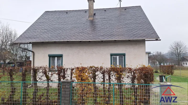 Vorderansicht des Hauses mit Satteldach, grünen Fensterläden und einer gepflegten Hecke.
