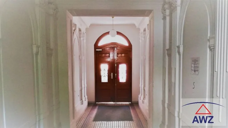 Heller Eingangsbereich mit hohen Decken, Stuckelementen und einer großen Holztür.