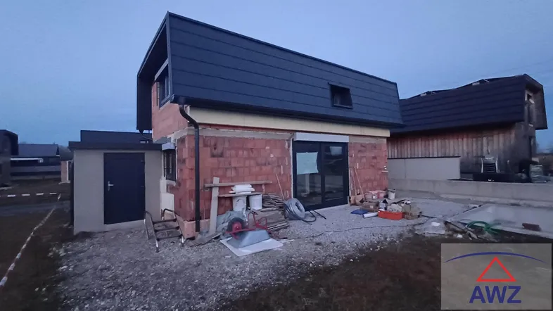 Neubauhaus im Rohbauzustand mit Dach und Fenstern, umgeben von Baustellenmaterialien.