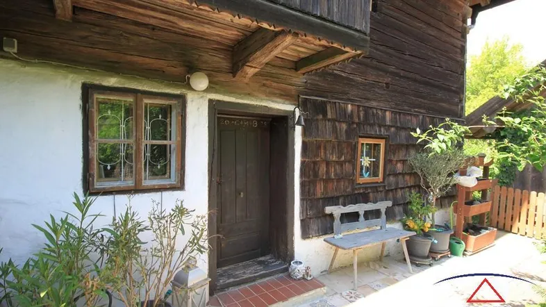 Traditioneller Hauseingang eines Holzhauses mit Holzbalkon, alten Fenstern und rustikaler Holzfassade.