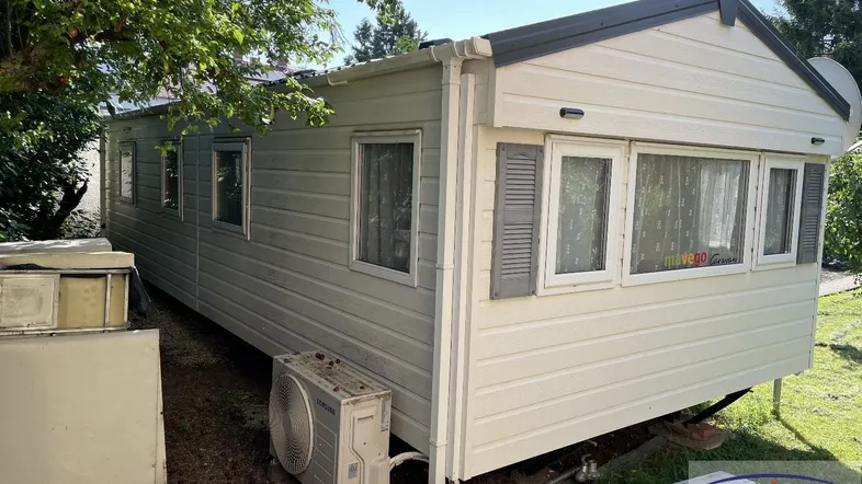 Außenansicht eines mobilen Hauses oder Chalets mit heller Fassade und Klimaanlage.
