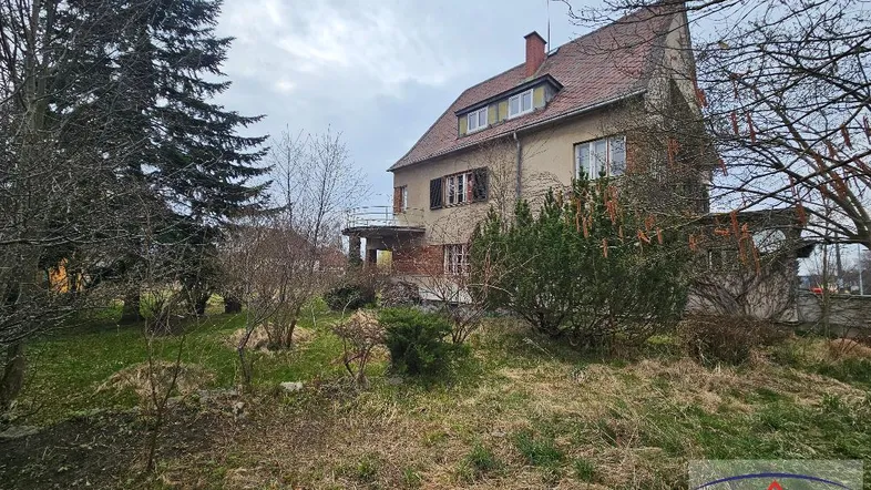 Altes Wohnhaus mit großem, naturbelassenem Garten unter bewölktem Himmel.