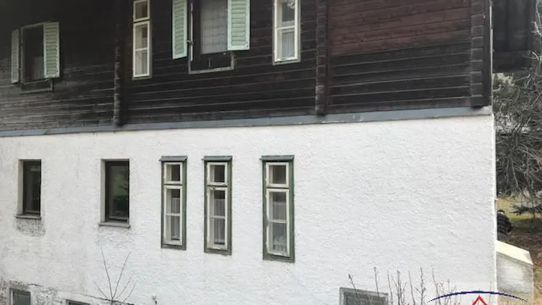 Fassade eines traditionellen Holzhauses mit weiß verputztem Sockel und grünen Fensterläden.