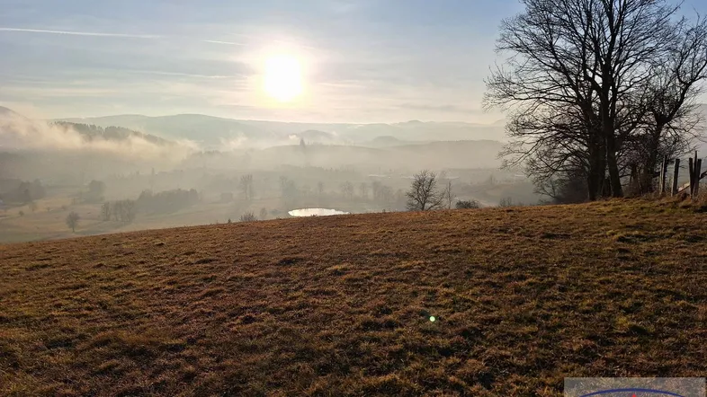 Malerische Landschaft mit sanften Hügeln, Nebelschwaden und einem See im Sonnenlicht.