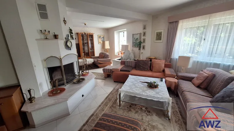 Geräumiges Wohnzimmer mit Kamin, Fliesenboden und traditioneller Einrichtung, offen zu einem weiteren Bereich.