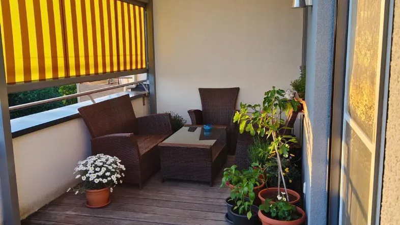 Überdachter Balkon mit Holzboden, bequemen Loungemöbeln und gelb-weiß gestreifter Markise für sonnige Stunden.