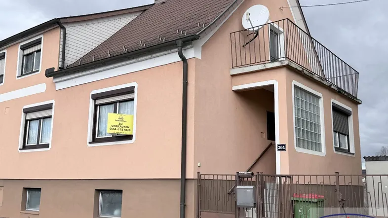 Einfamilienhaus mit hellrosa Fassade, Satteldach und kleinem Balkon im Obergeschoss.