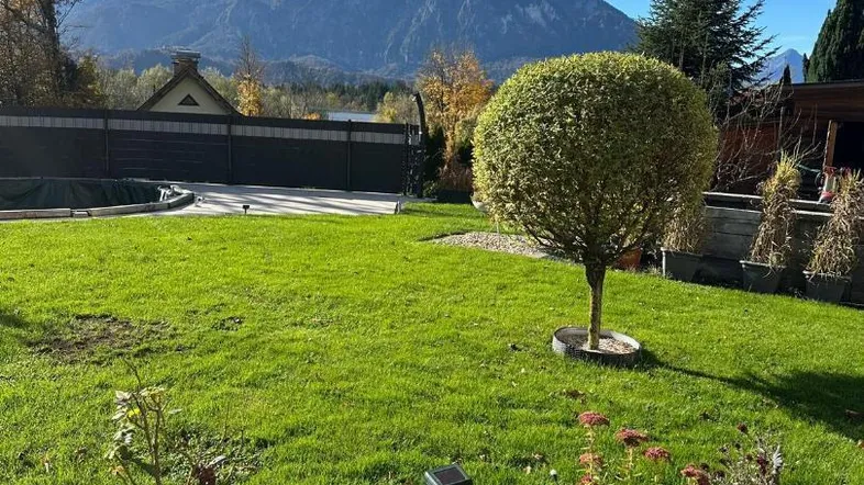 Großer grüner Garten mit gepflegtem Rasen, Blumenbeeten und beeindruckendem Bergblick.