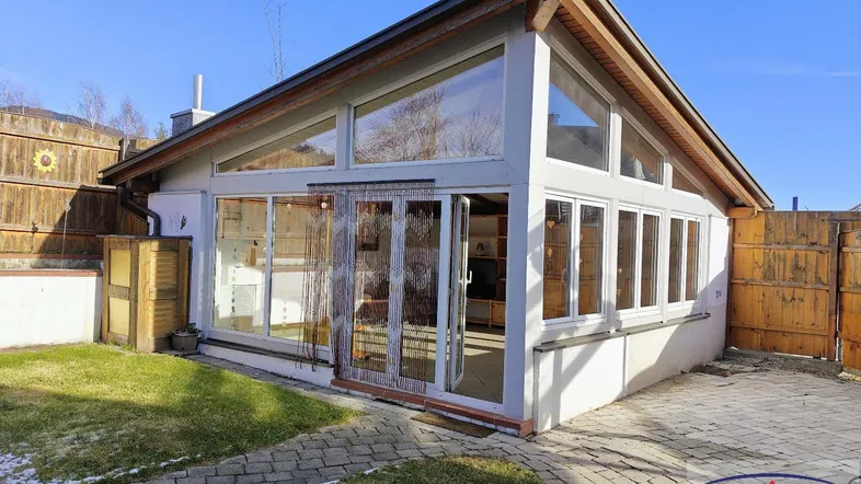Modernes Gebäude mit großen Glasflächen und Holzdetails, umgeben von Rasen und gepflastertem Bereich.