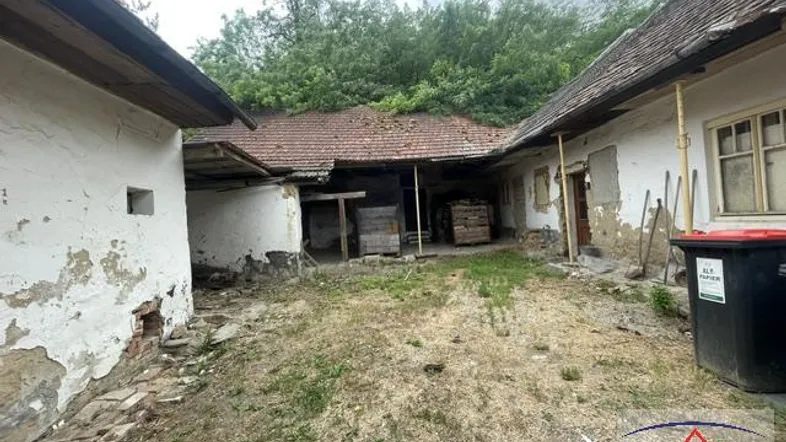 Verfallener Innenhof zwischen alten Gebäuden mit bröckelndem Putz und bewachsenem Dach.