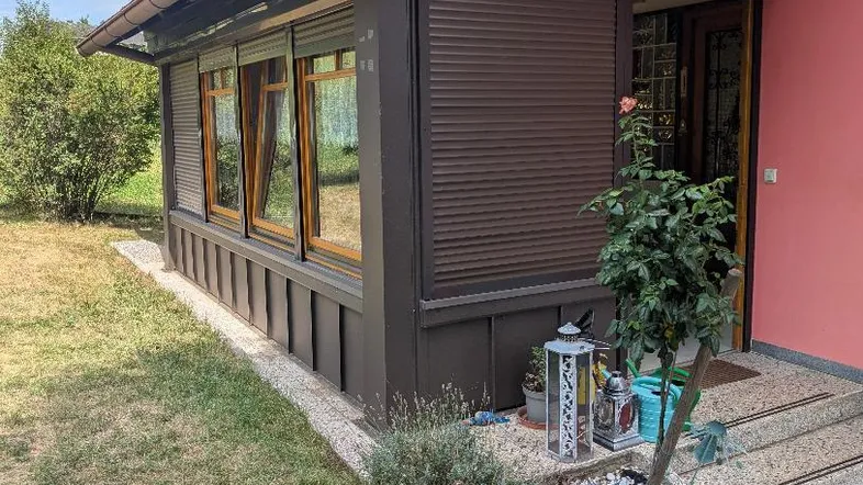 Anbau mit Wintergarten und geschlossenen Rollläden, umgeben von einem gepflegten Gartenbereich.