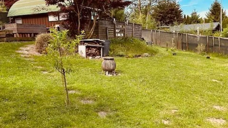 Großer Gartenbereich mit Rasenfläche, Bäumen und einer Feuerstelle vor einer Holzhütte.