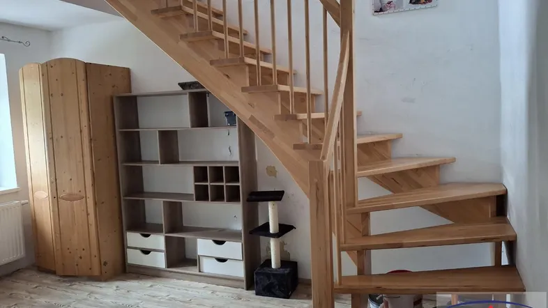 Helles Zimmer mit Holztreppe, Regalen und Schrank, ideal als Wohn- oder Flurbereich.