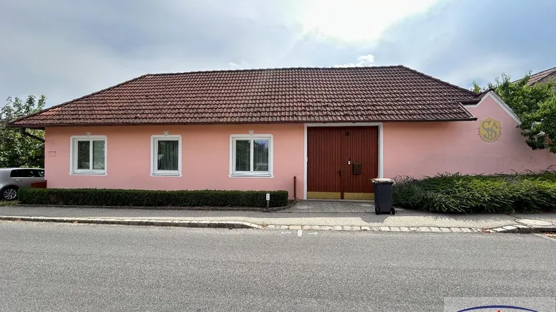 Rosa Hausfassade mit braunem Ziegeldach und großer Garagentür an der Vorderseite.