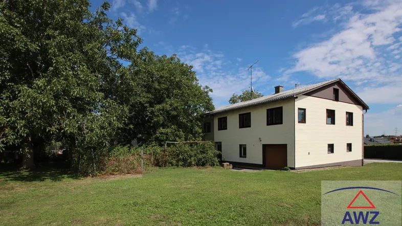 Einfamilienhaus mit großem Garten und altem Baumbestand unter blauem Himmel.