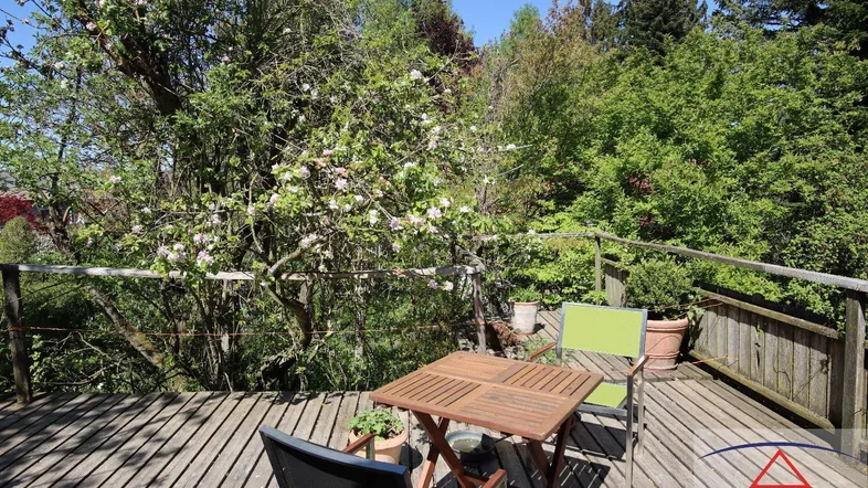 Geräumige Holzterrasse mit Gartenmöbeln und üppigem Grünblick, umgeben von blühenden Bäumen.