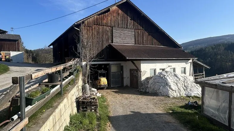 Rustikales Bauernhaus mit Holzbalken und weißem Anbau, umgeben von ländlicher Landschaft unter blauem Himmel.