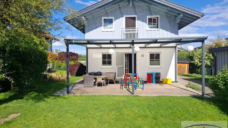 Modernes Einfamilienhaus mit überdachter Terrasse, Garten und Balkon im Obergeschoss.