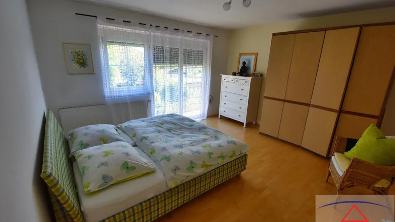 Helles Schlafzimmer mit Doppelbett, Holzschrank und Zugang zum Balkon oder Garten.