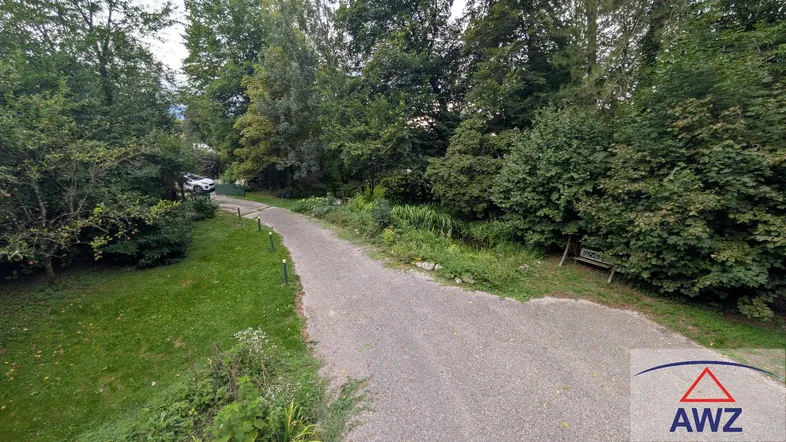 Schotterweg führt durch eine grüne, baumbestandene Landschaft mit viel Natur.