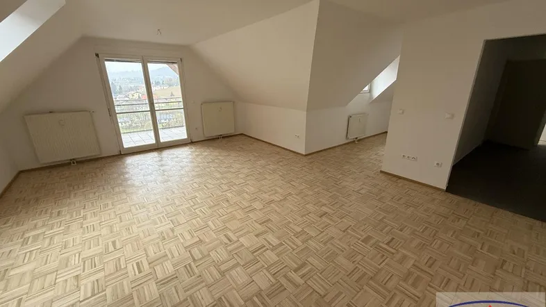 Geräumiger Wohnbereich im Dachgeschoss mit Parkettboden und Zugang zum Balkon.