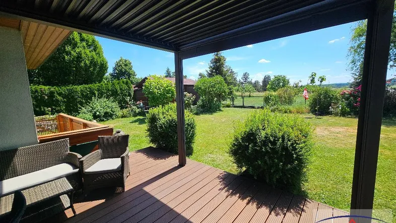 Überdachte Terrasse mit Holzdeck und Gartenmöbeln, bietet einen weiten Blick ins Grüne.