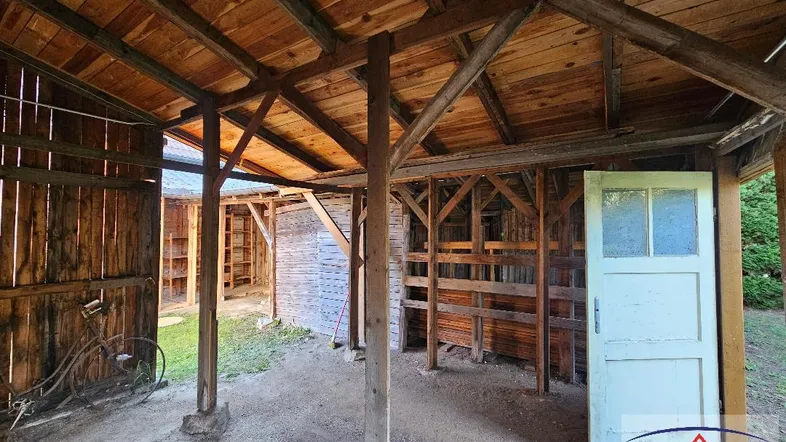 Rustikaler Holzunterstand mit offener Bauweise und Erdboden, ideal als Lagerraum oder Carport.
