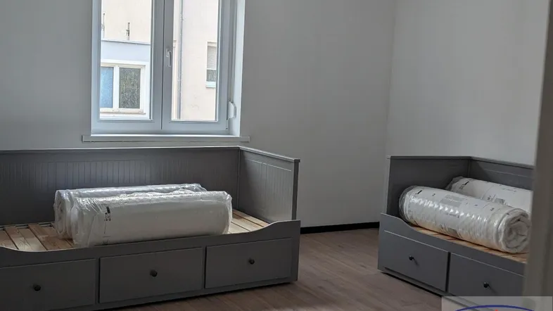 Helles Schlafzimmer mit zwei grauen Tagesbetten und Laminatboden, ideal für Gäste oder Kinder.