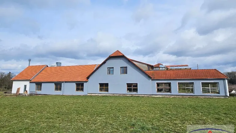 Langes Gebäude mit hellblauer Fassade, roten Ziegeldächern und weitem Blick auf die Landschaft.