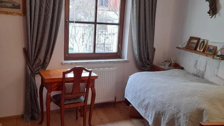 Gemütliches Schlafzimmer mit Holzboden, kleinem Schreibtisch und traditioneller Einrichtung am Fenster.