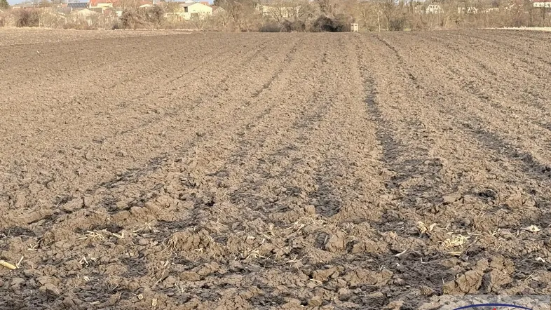 Weites, gepflügtes Feld mit Blick auf die entfernte Bebauung unter bewölktem Himmel.