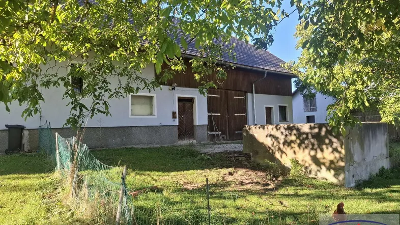 Altes Bauernhaus mit Scheunentor und großem Gartenbereich unter Bäumen an einem sonnigen Tag.