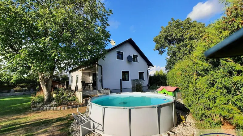 Gartenbereich mit oberirdischem Pool, umgeben von Bäumen und Grünflächen unter blauem Himmel.