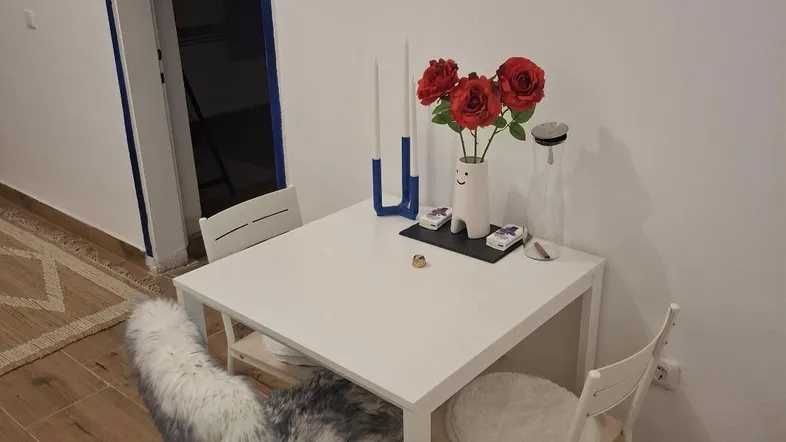 Kleiner Essbereich mit weißem Tisch, Stühlen und dekorativen roten Blumen.