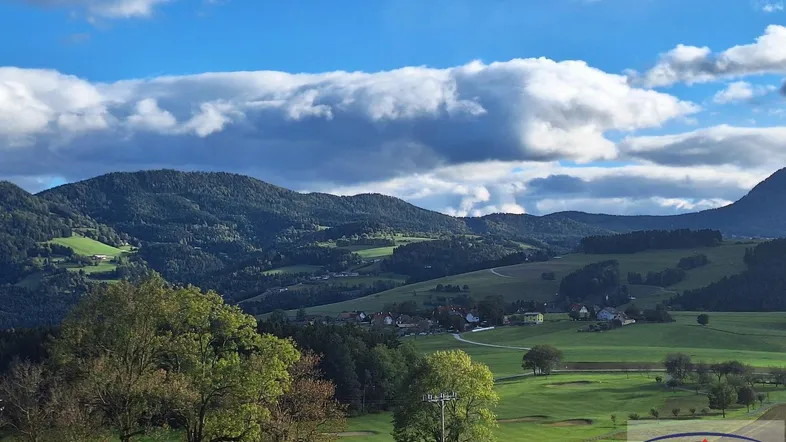 Malerische Landschaft mit grünen Hügeln, Bergen im Hintergrund und einem kleinen Dorf.