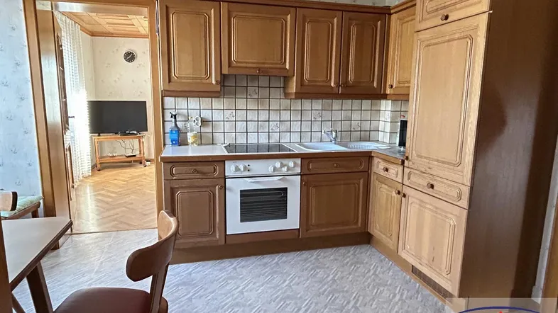 Traditionelle Küche mit Holzschränken, Fliesenrückwand und Blick in ein angrenzendes Zimmer.