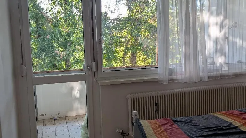 Helles Schlafzimmer mit Parkettboden, Zugang zum Balkon und Blick ins Grüne.