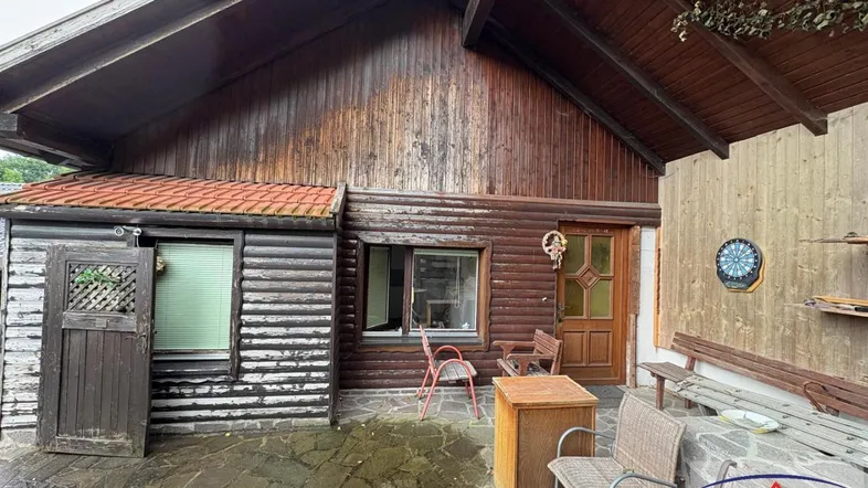 Rustikale Holzfassade eines Hauses mit gepflasterter Terrasse und Sitzgelegenheiten im Freien.