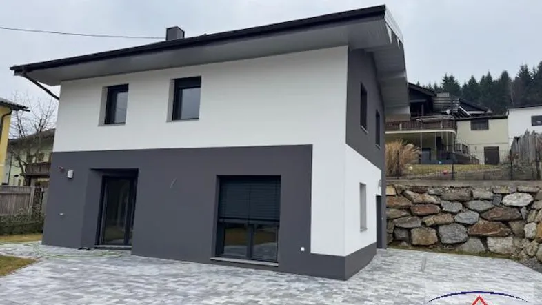 Modernes Einfamilienhaus mit weißer und grauer Fassade, gepflasterter Zufahrt und Natursteinmauer.