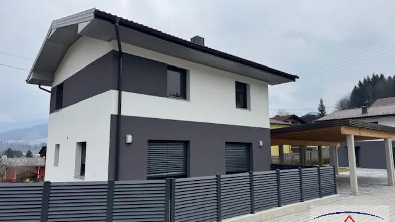 Modernes Einfamilienhaus mit zweifarbiger Fassade, Zaun und Carport im Vordergrund.