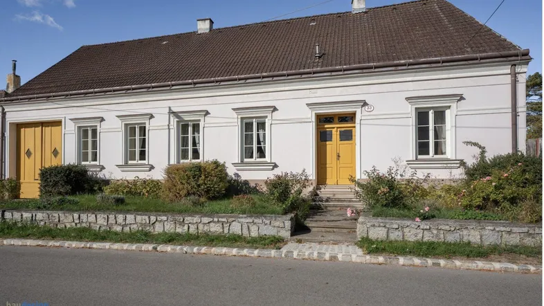 Traditionelles Einfamilienhaus mit weißer Fassade, gelben Türen und Satteldach.