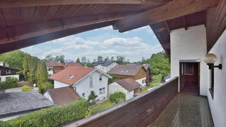 Geräumiger Balkon mit Holzbalken und Blick auf die umliegende Wohngegend und grüne Hügel.