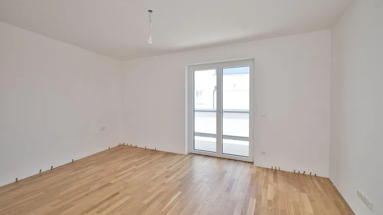 Helles, leeres Zimmer mit neuem Parkettboden und Zugang zu einem Balkon oder einer Terrasse.