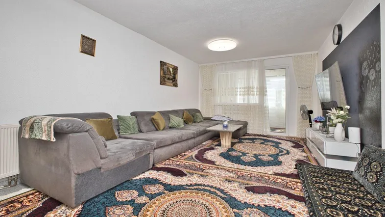 Geräumiges Wohnzimmer mit großem Ecksofa, gemustertem Teppich und Zugang zum Balkon.
